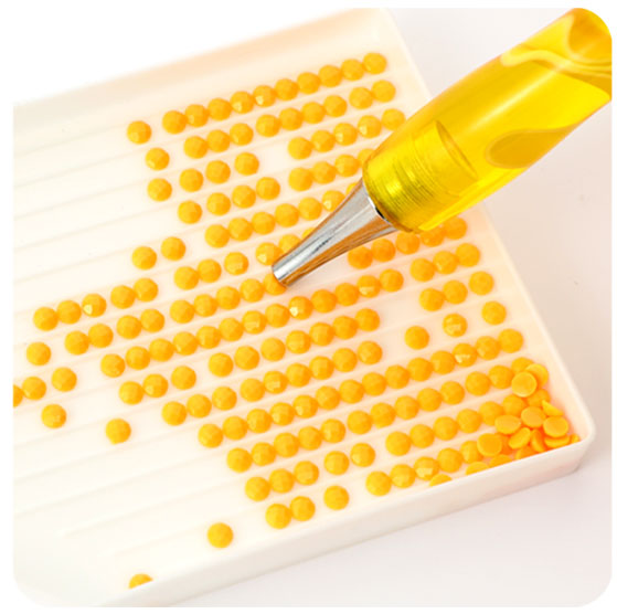 Step 3 of how to do diamond painting: pouring diamond drills into a tray and using the wax-filled pen to pick up each drill.